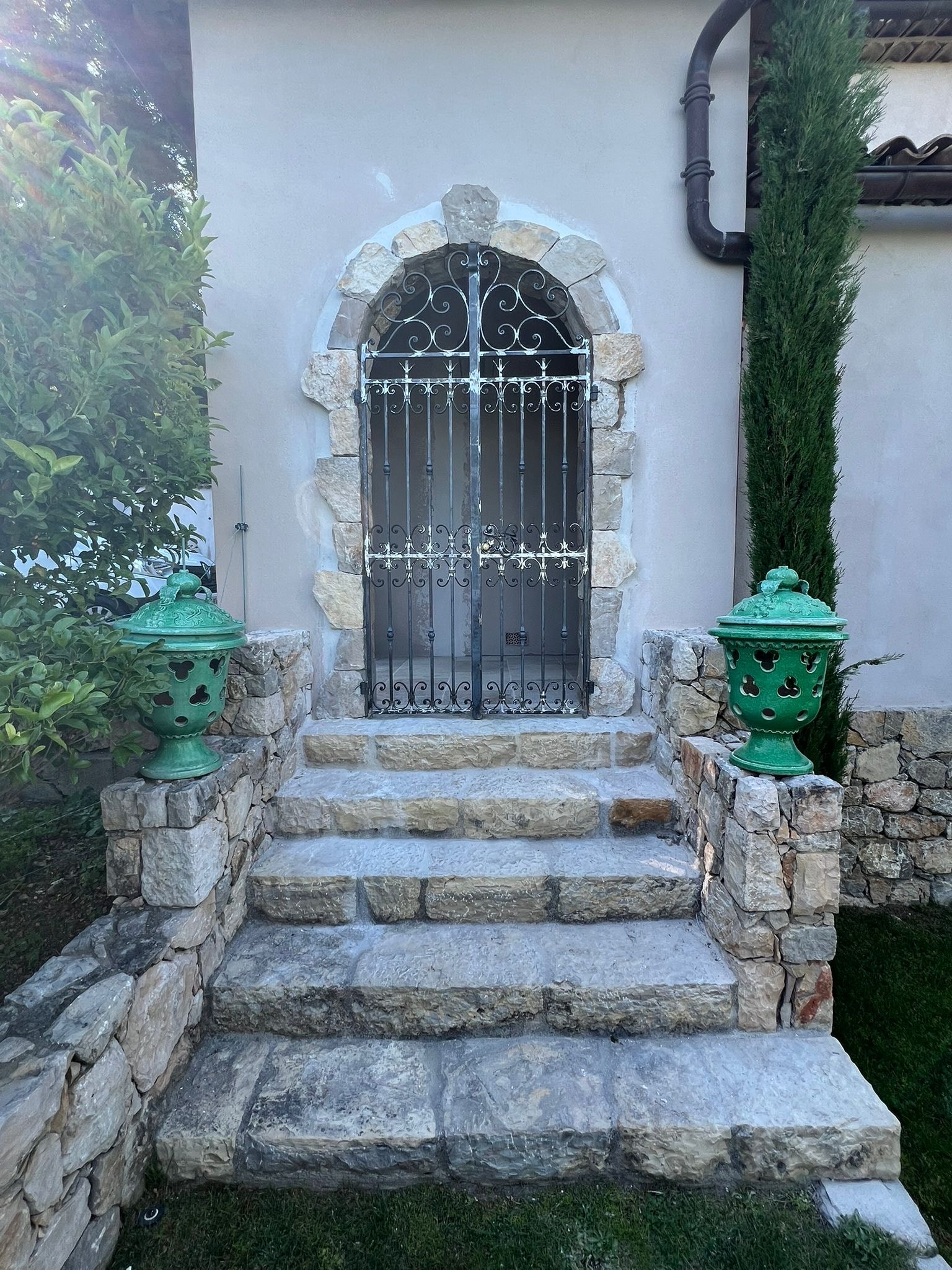 Grille-porte en fer forgé cintrée sur un perron en pierre, encadrée d'un appareillage de pierre de taille